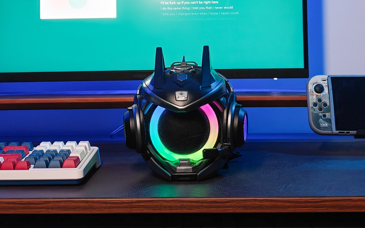 Black OLLIE speaker with a glowing RGB ring between a keyboard and handheld console